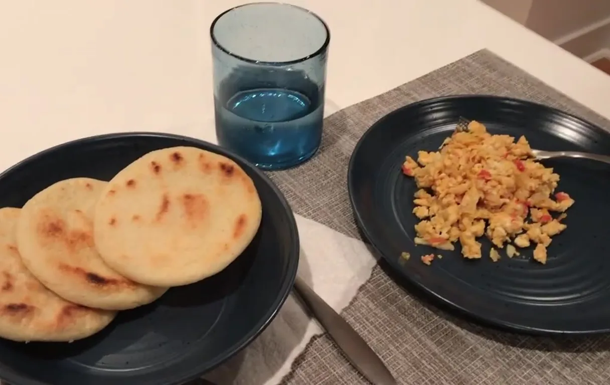 Three golden arepas on a plate beside a plate of huevos pericos, scrambled eggs with tomato and onion, in Gredivel Vasquez's kitchen