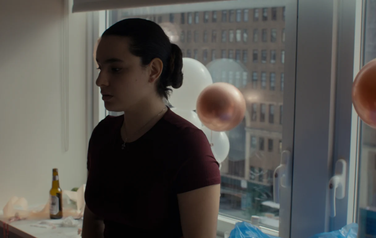 Cristina Villalobos as the hotel maid standing in a guest room strewn with party balloons in the short film In Sanctuary