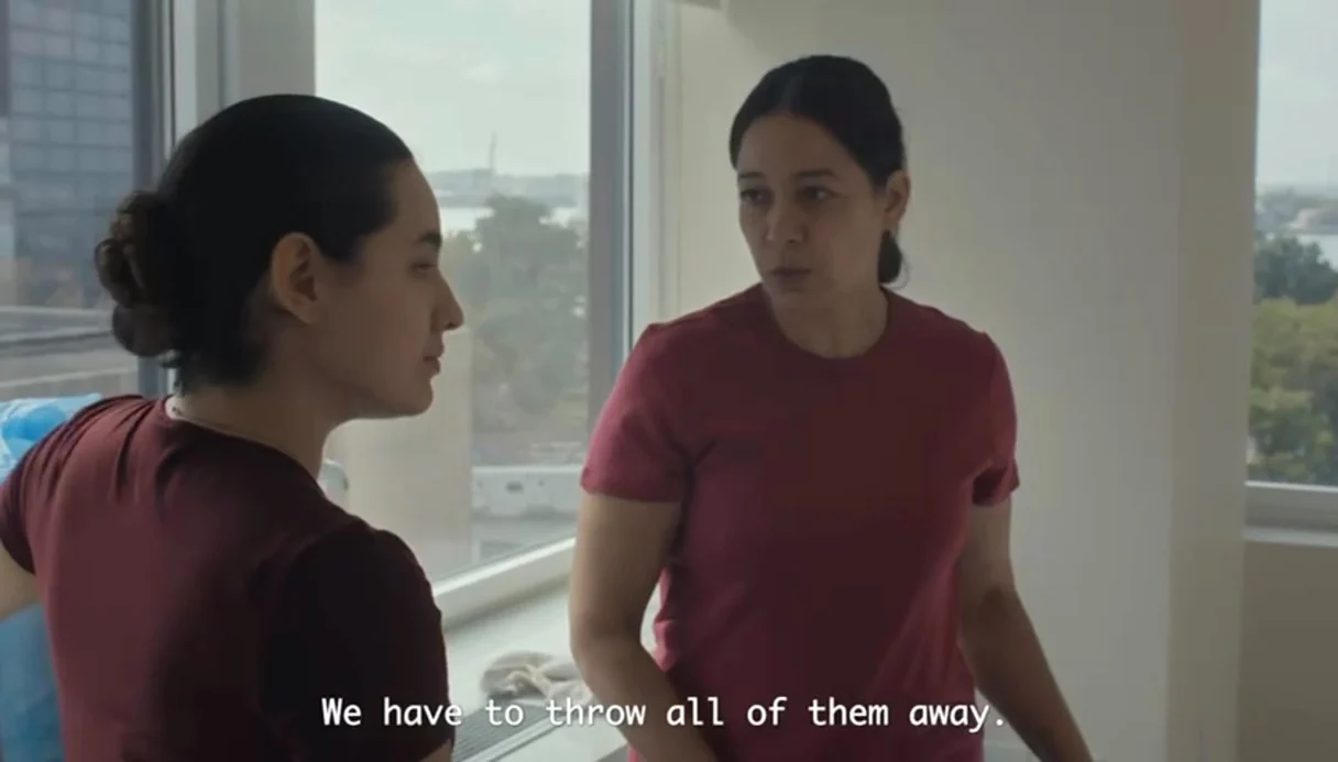 Gredivel Vasquez as Ximena speaking to Cristina Villalobos as Camila by a high-rise hotel window in the 2026 short film In Sanctuary, subtitle reading We have to throw all of them away