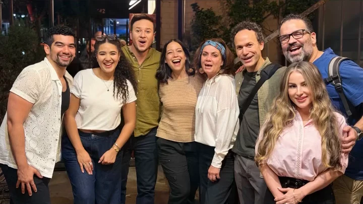 The cast of La Gringa standing together and laughing on the sidewalk outside Repertorio Espanol in New York at night